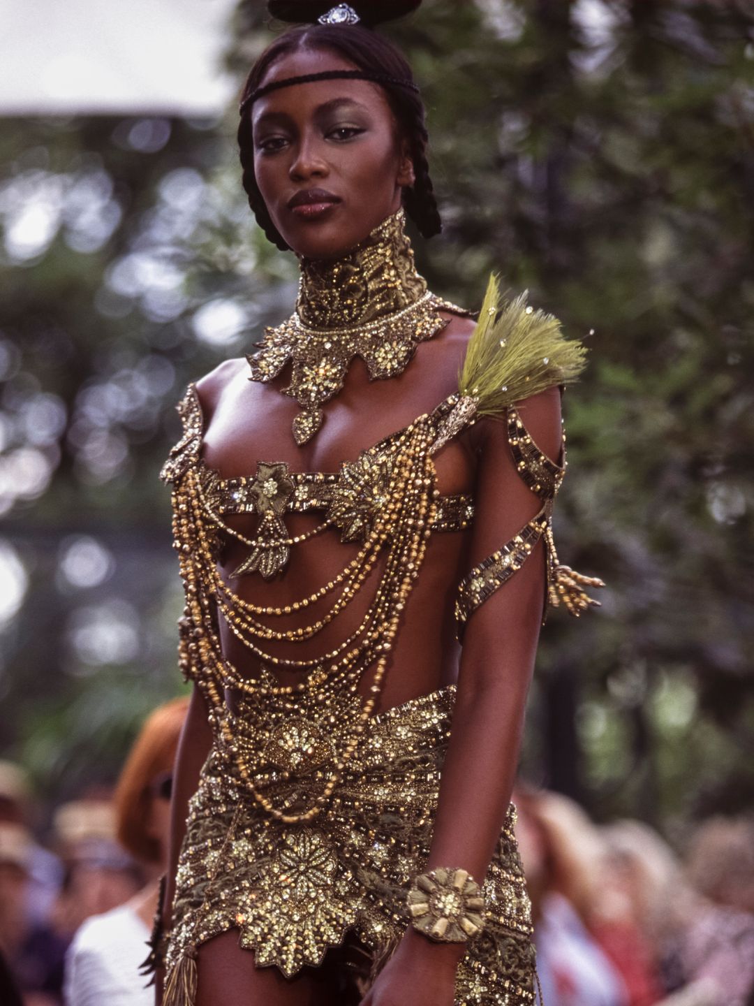 Naomi Campbell wearing a gold beaded micro top with layered necklaces 
