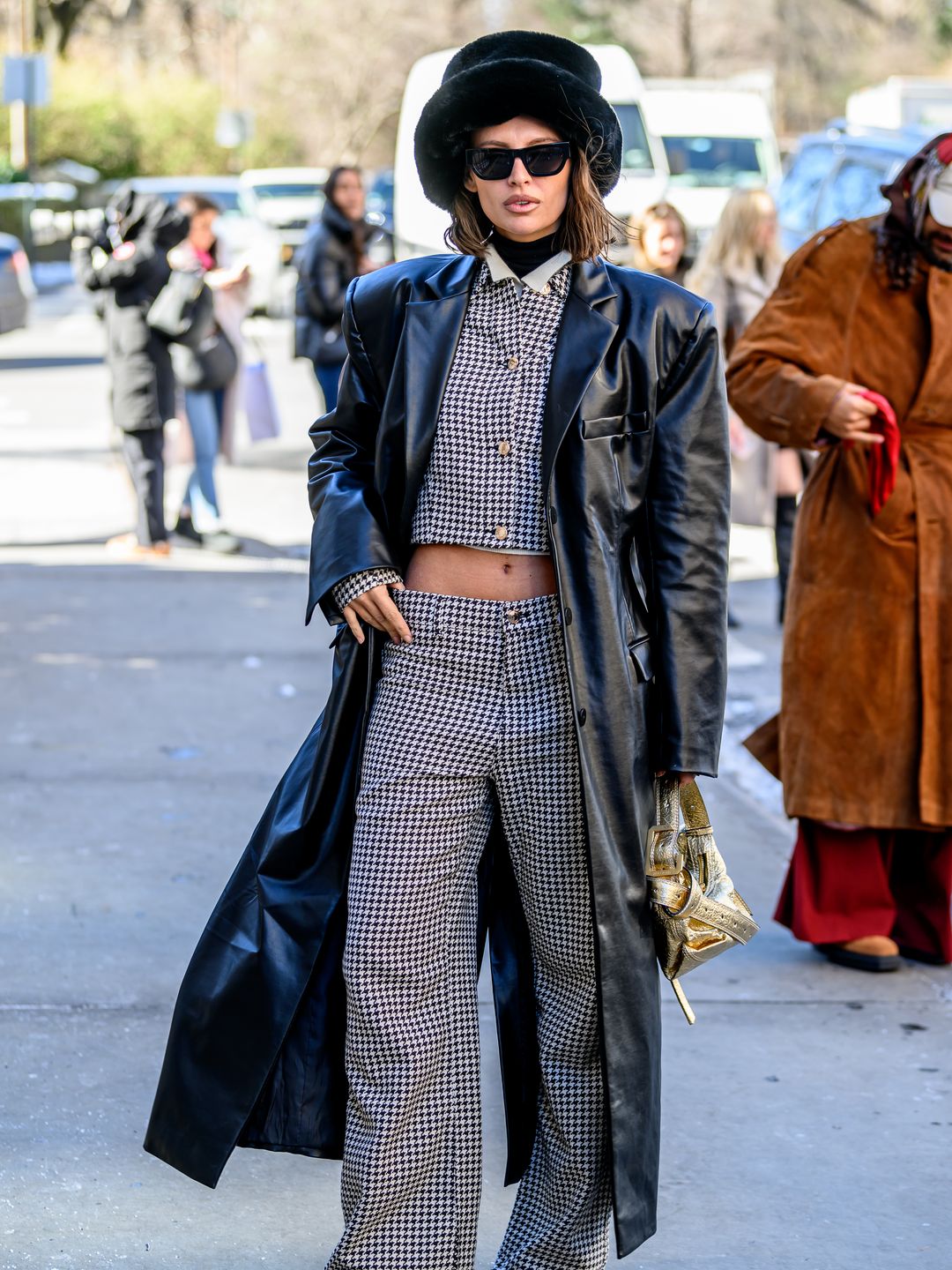 rina Kro Eicke wears a black coat, and a checkered pants and top set as she poses outside the Bevza Fashion Show 