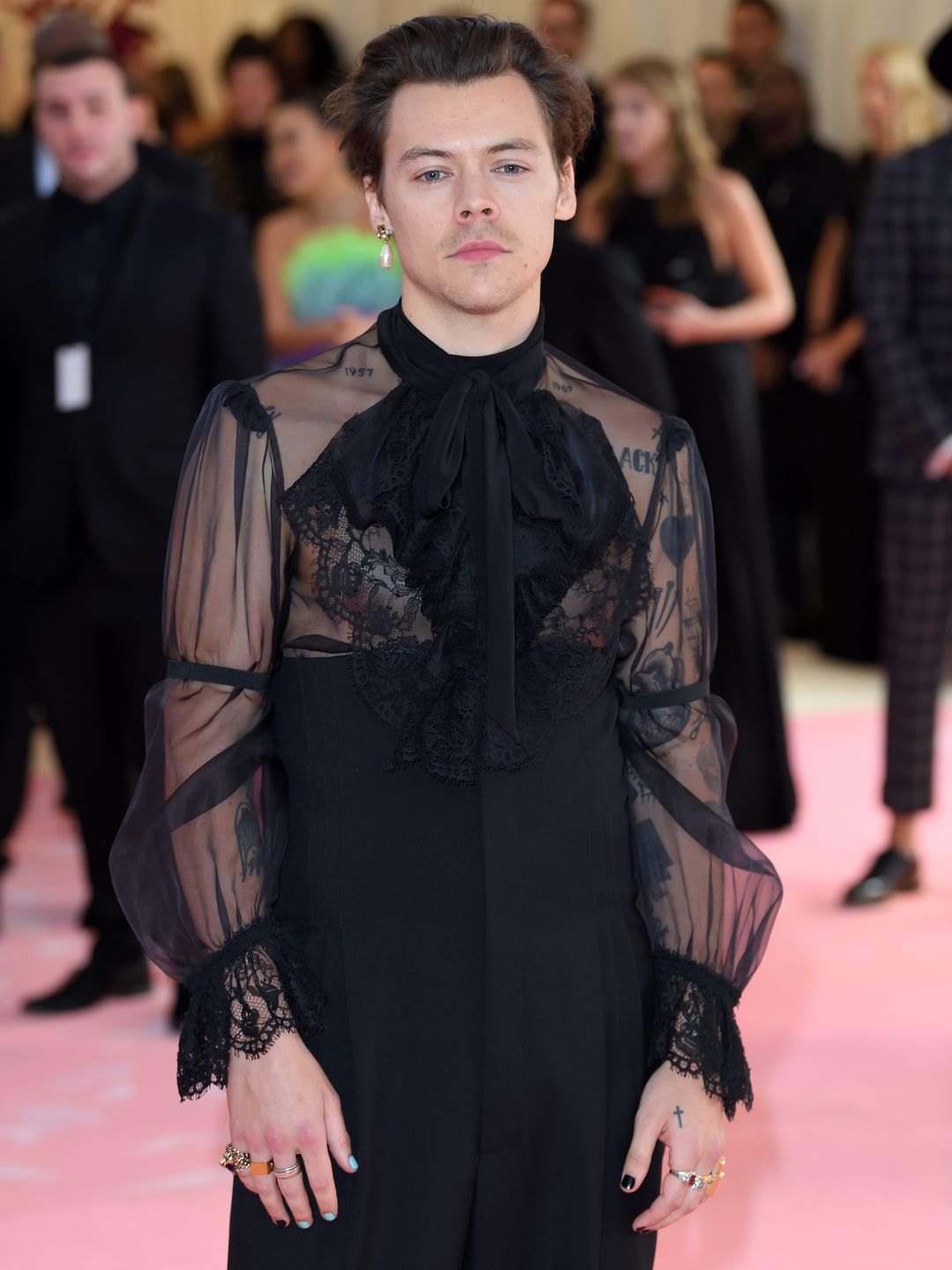 Harry Styles arrives for the 2019 Met Gala wearing a lace black jumpsuit and single pearl earring