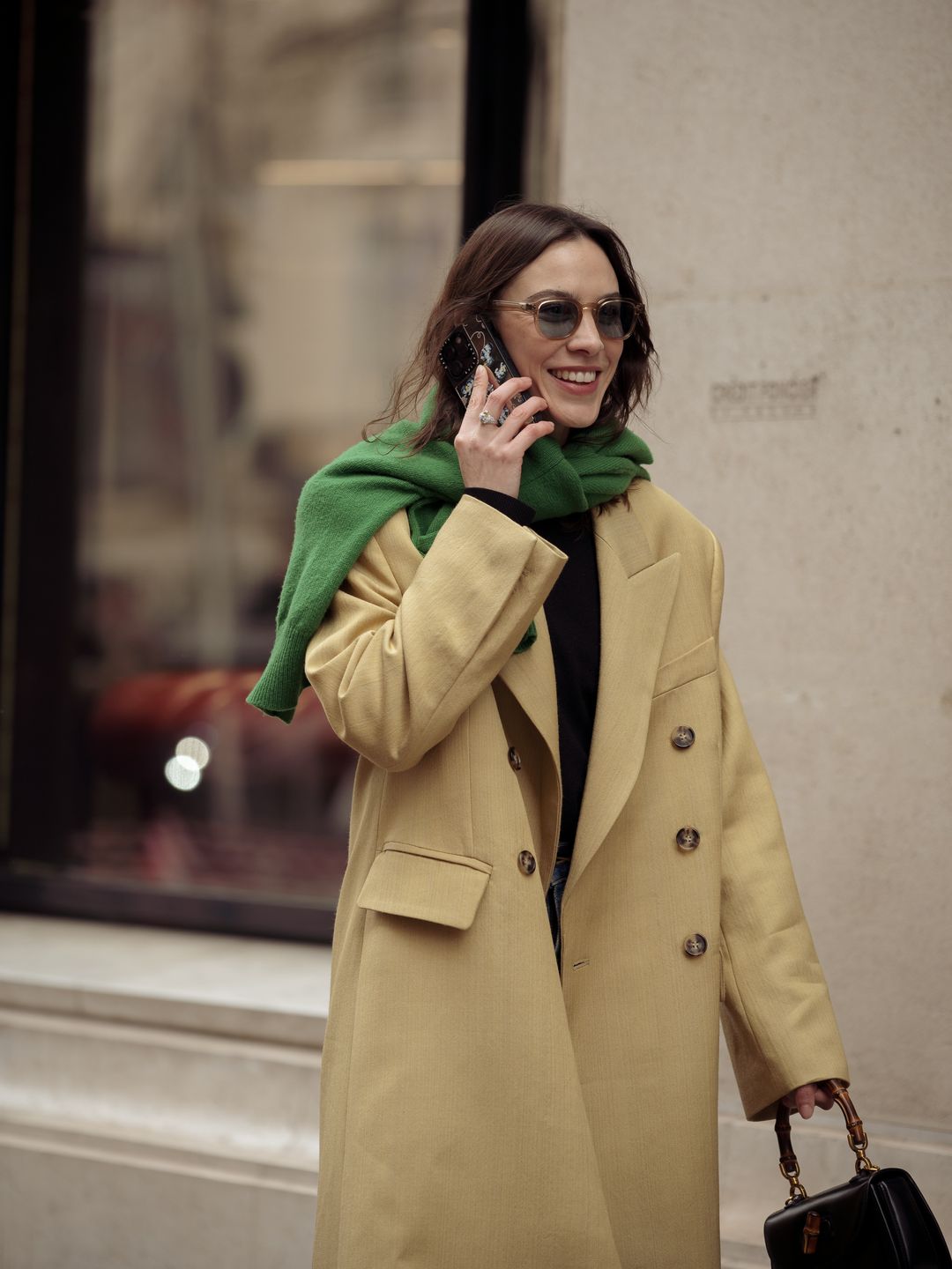 Alexa Chung wears blue jeans, beige coat and green sweater over the shoulders outside The Row during the Womenswear Fall/Winter 2024/2025 as part of  Paris Fashion Week