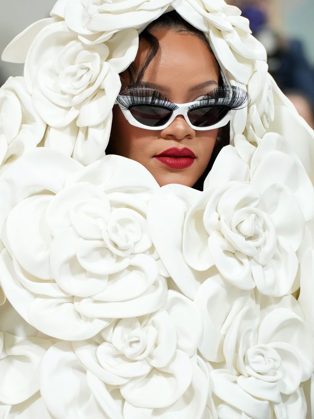 Rihanna attends the 2023 Met Gala in a rose adorned white cape and white sunglasses with false lashes