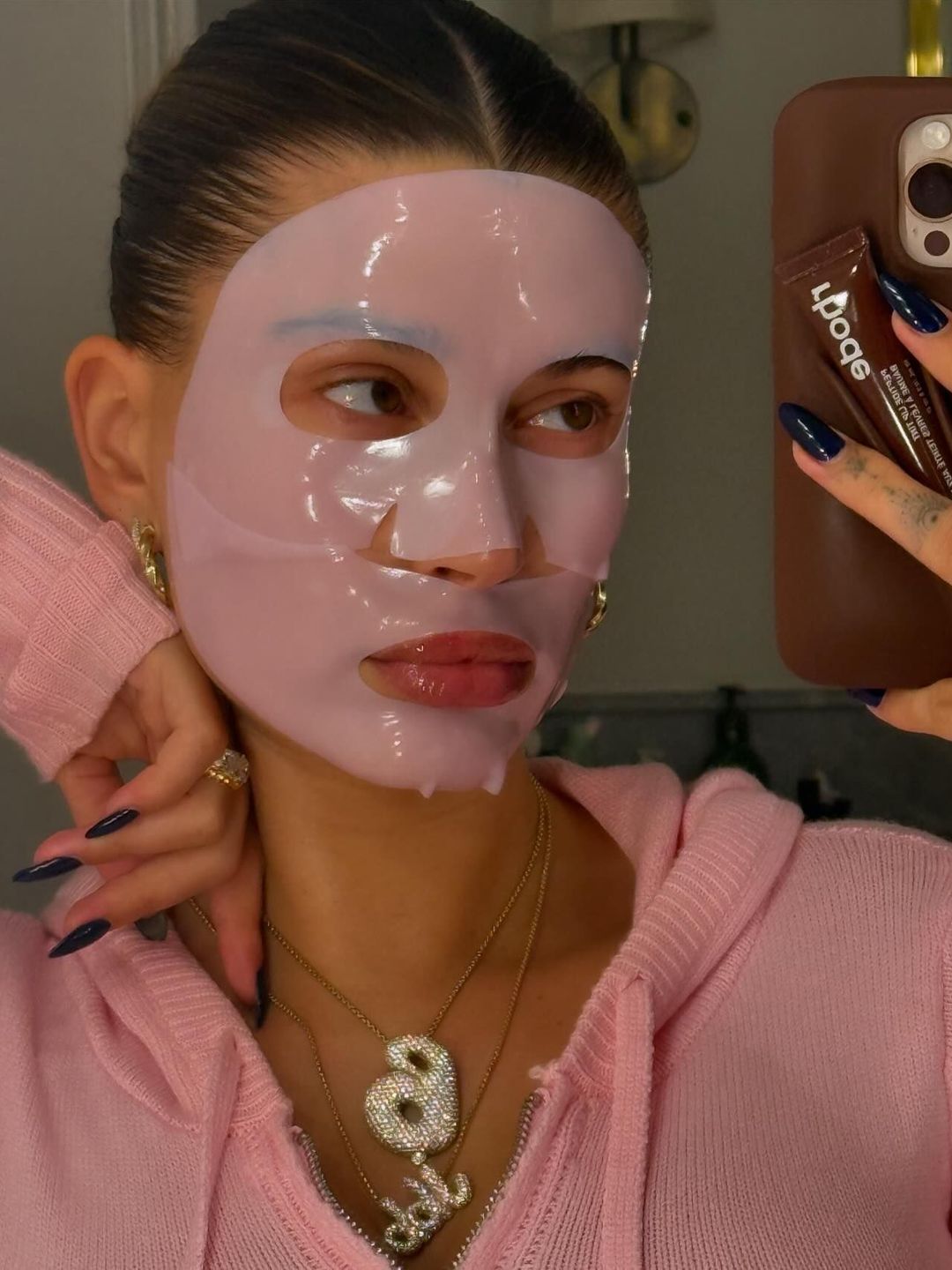 Hailey Bieber shares a mirror selfie of herself wearing a pink jumper and a matching face mask