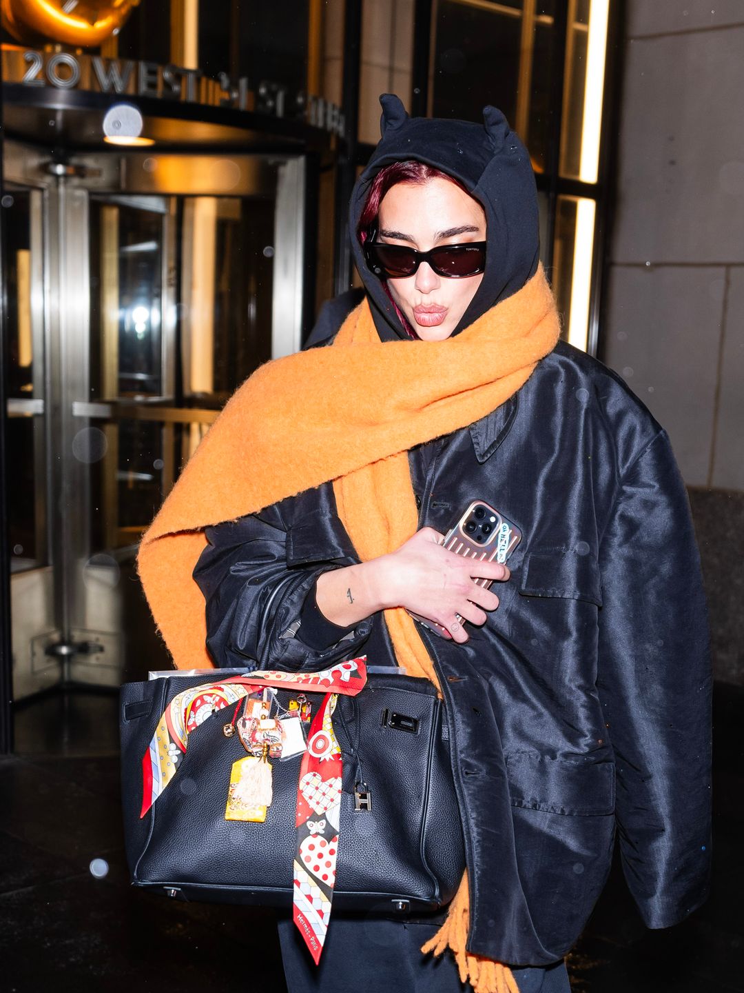 Dua Lipa is seen in NYC wearing a black sweat suit and orange scarf 