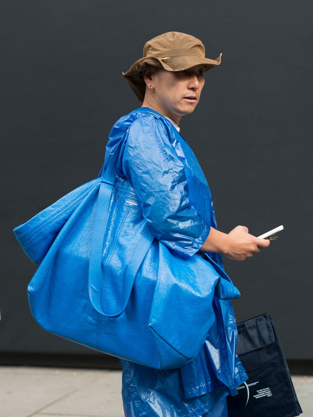 A guest of Balenciaga's 2017 show wears a blue coat and matching blue bag with a brown hat