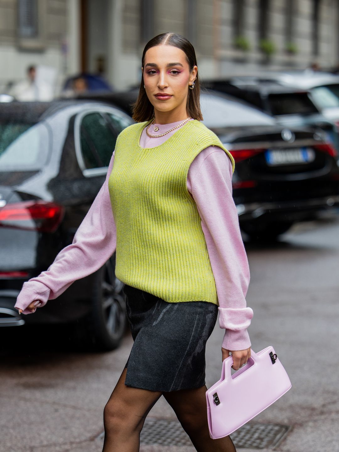 Ginevra Mavilla wears pink bag, shirt, mini skirt with slit, tights, green sleeveless knit outside Onitsuka Tiger during the Milan Fashion Week Menswear Spring/Summer 2025 on September 18, 2024 in Milan, Italy.