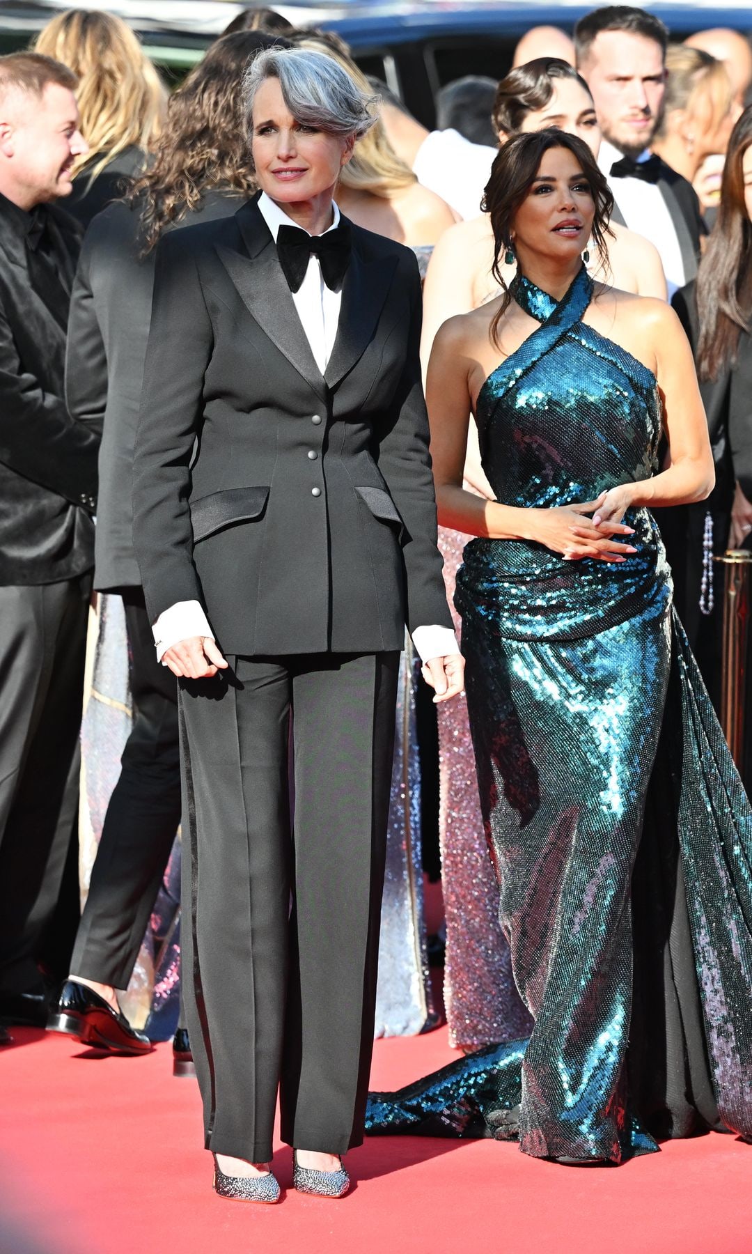Andie McDowall in a black tuxedo standing with Eva Longoria in a halterneck green dress