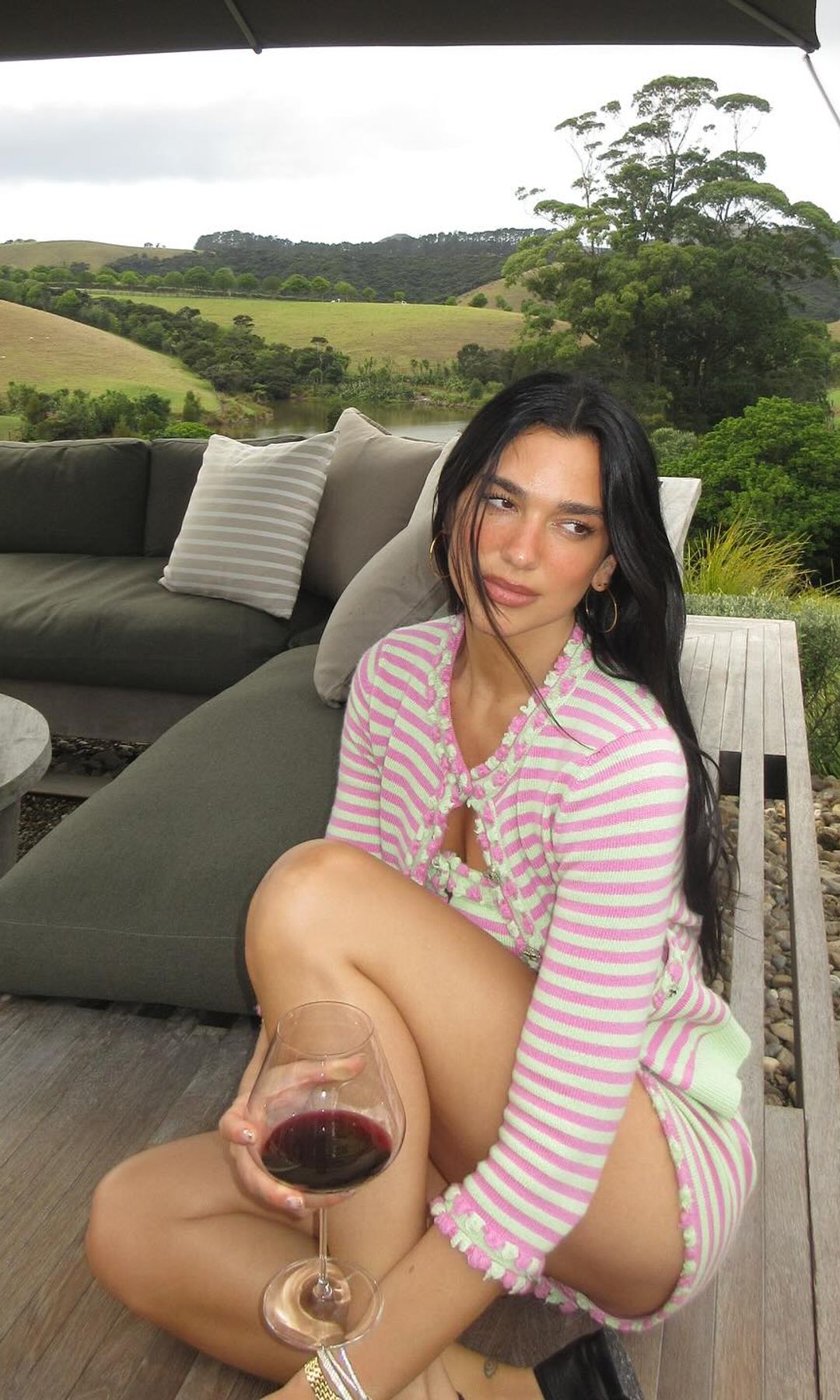 Dua Lipa poses in a green and pink striped Chanel look while sipping on a red wine in New Zealand