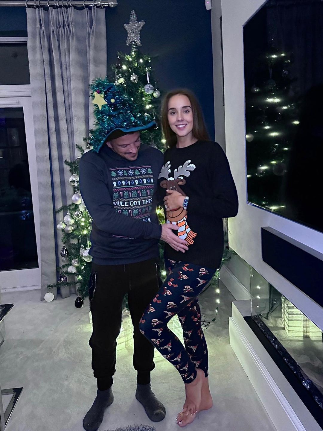 Emily and Peter Andre cradle her baby bump by the Christmas tree