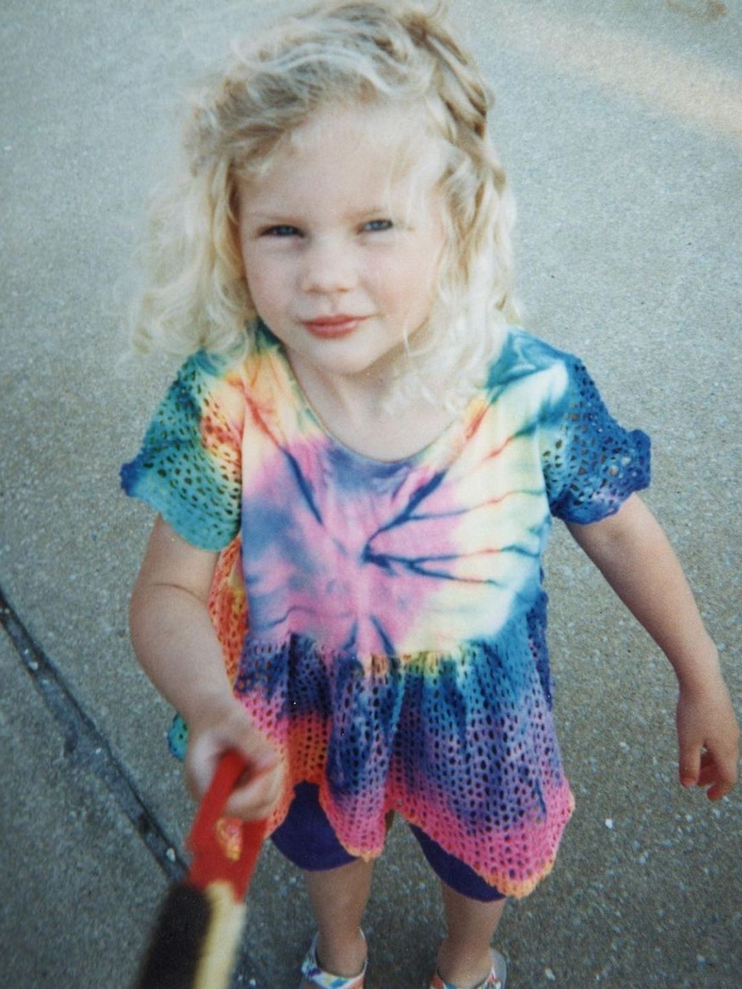A young Taylor Swift smiling in a tiedye shirt
