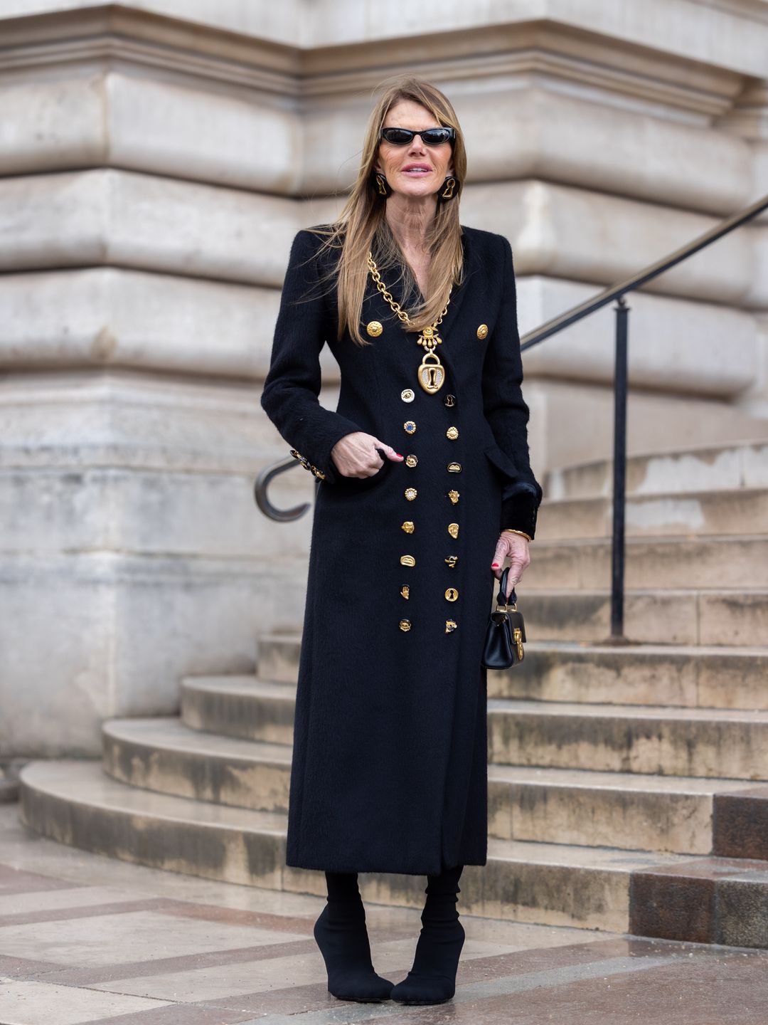 Anna Dello Russo attends the Schiaparelli Haute Couture Spring/Summer 2024 show wearing a fitted long black coat, black boots and black sunglasses