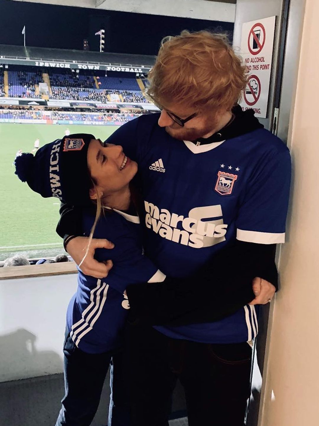 Ed and Cherry looking at eachother lovingly, photographed near a football pitch
