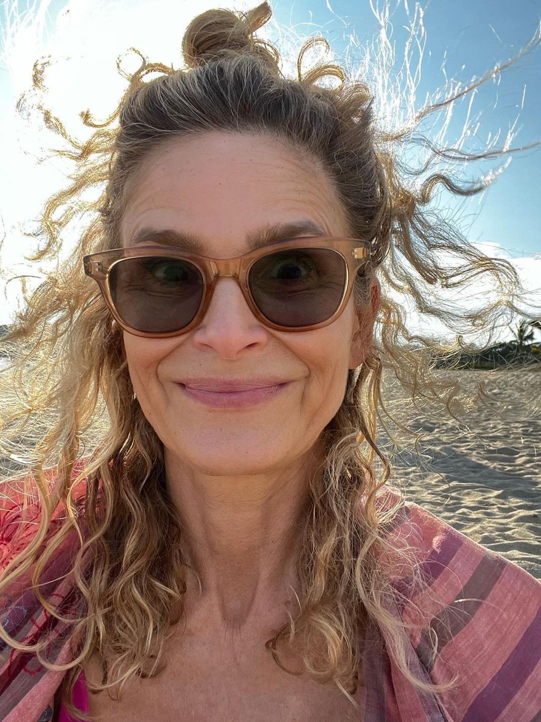 Kyra Sedgwick smiling at the camera with her blowing behind her at the beach