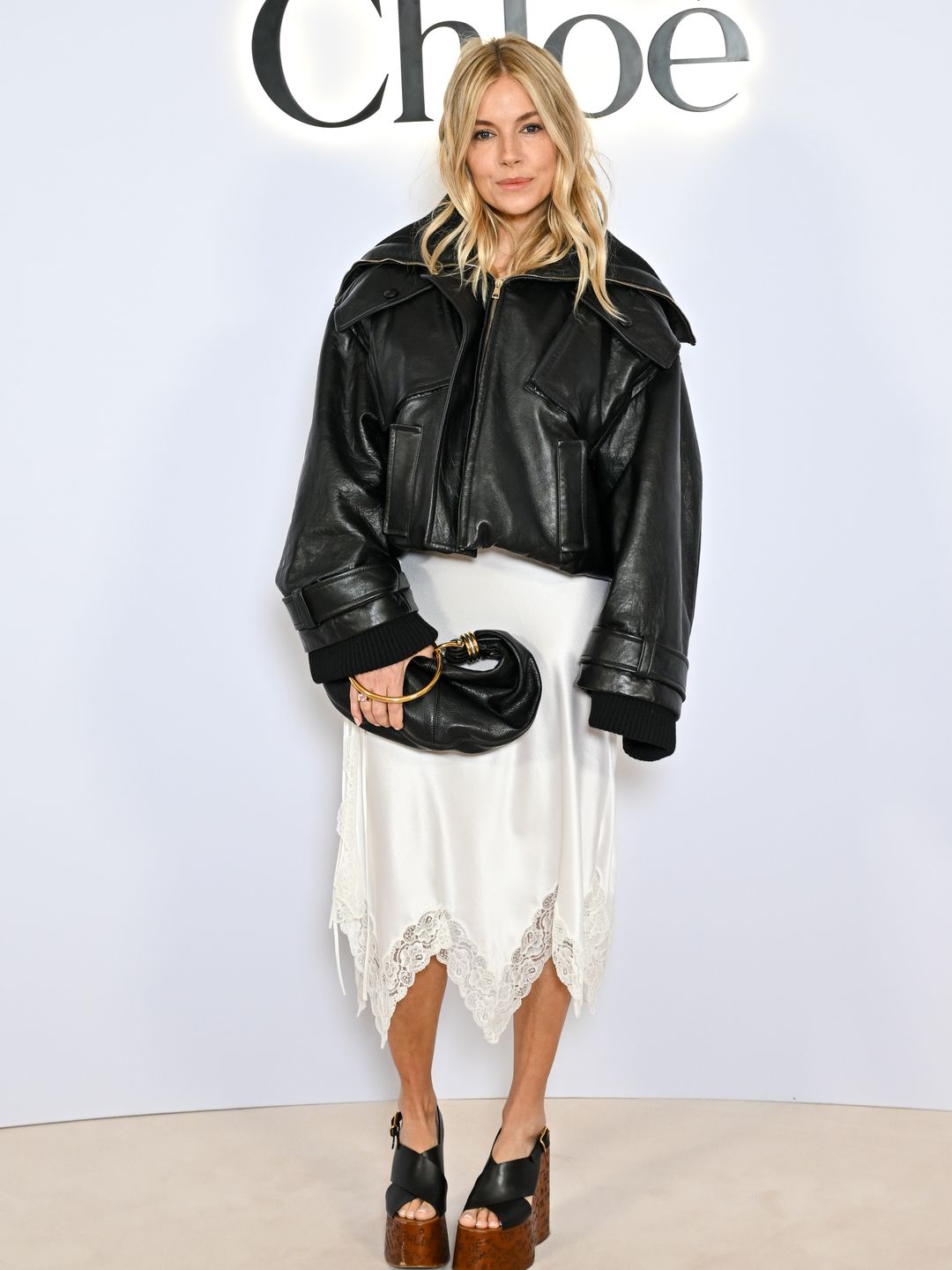 Sienna Miller looked chicer than ever in a white handkerchief slip dress and oversized leather jacket at the Chloé show.