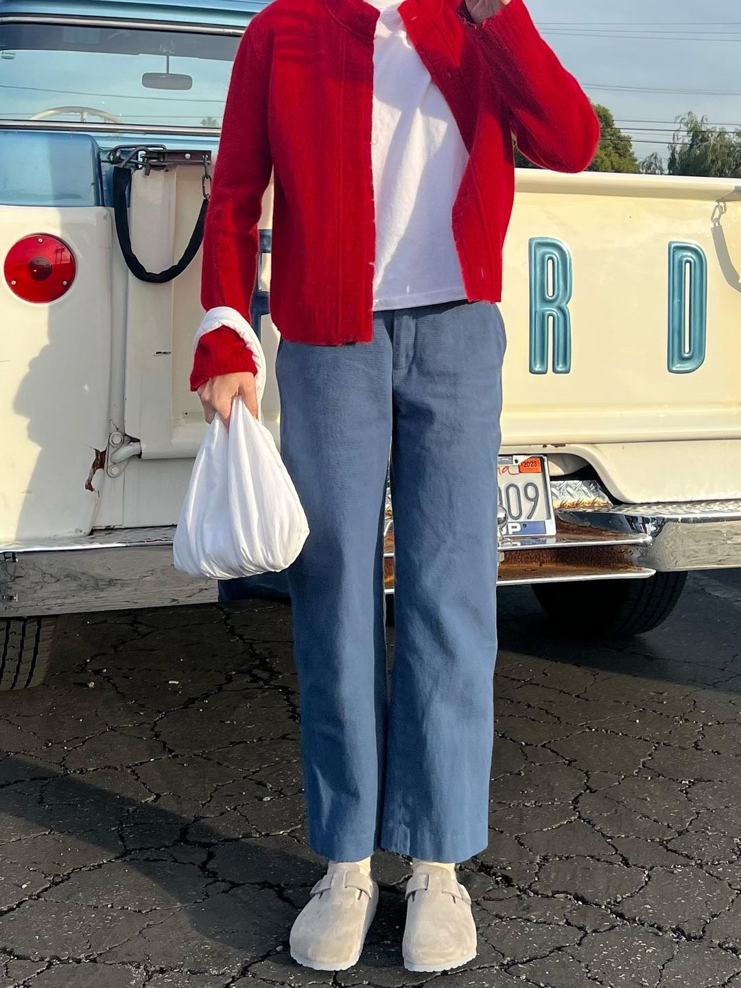 Emma Chamberlain shows off her casual outfit in front of a truck. Her outfit consists of slouchy trousers, Birkenstock Bostons, a white t-shirt and a red cardigan