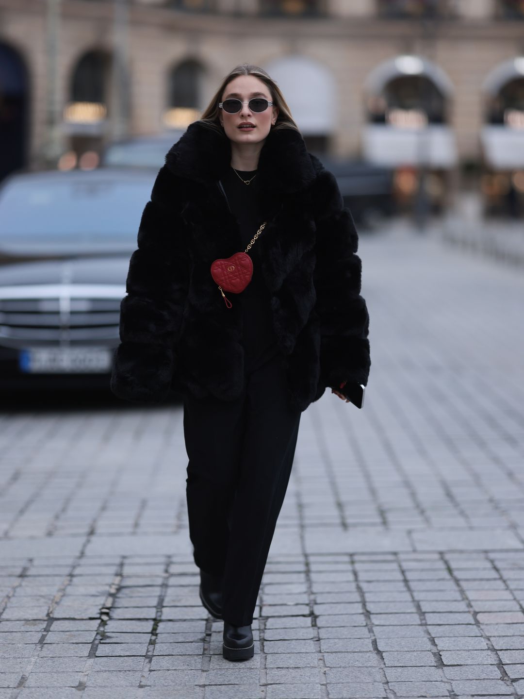 Andra Theobald seen wearing Celine silver oval Triomphe sunglasses, gold necklace, black wool knit sweater, Glamify Fashion black fake fur short coat, NA-KD black straight leg suit pants, Dior red leather heart shaped mini crossbody bag and Louis Vuitton black leather heeled boots,