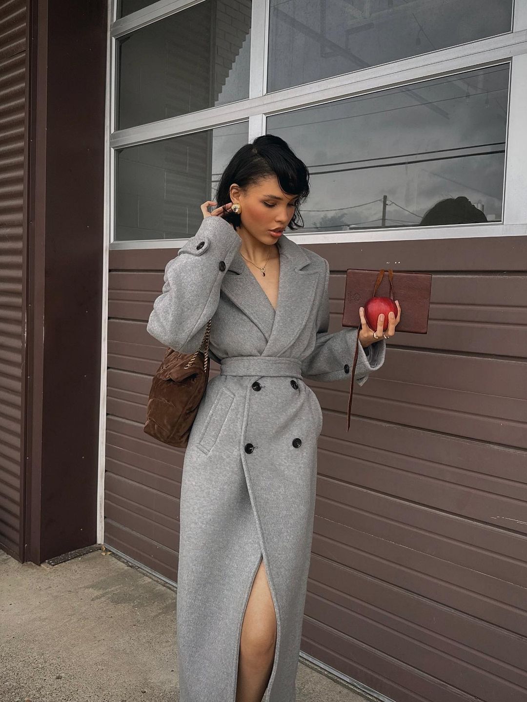 Nara Smith poses in a grey coat with an apple 