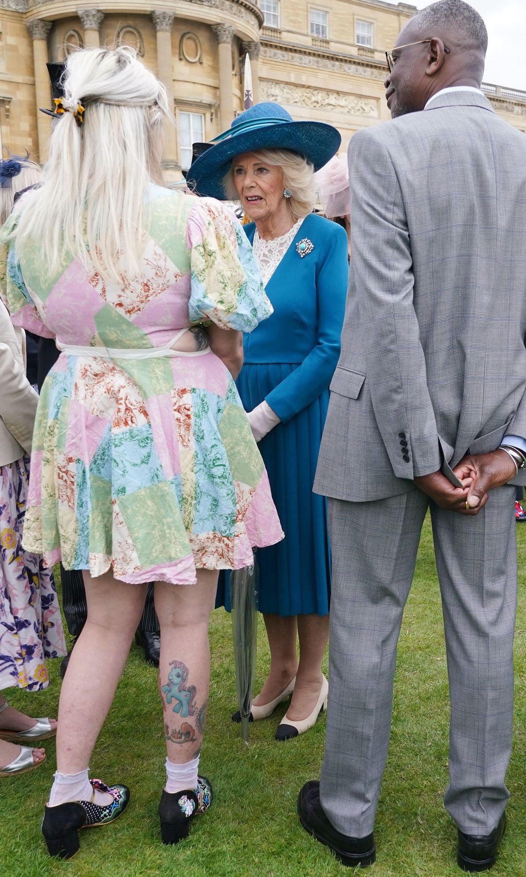 Queen Camilla talking to a woman in a mini dress with My Little Pony tattoos