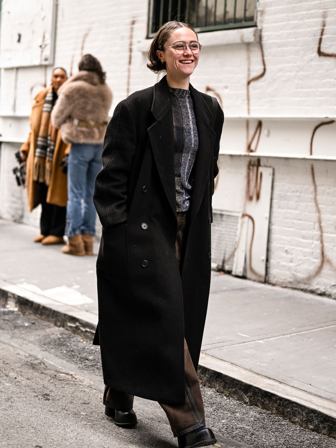 Ella Emhoff is seen wearing a black coat, gray and black Eckhaus Latta shirt, brown pants and black boots outside the Eckhaus Latta show during NYFW F/W 2025 on February 08, 2025 in New York City