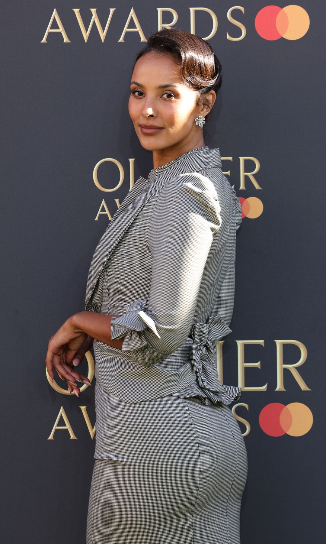 Maya Jama attends The Olivier Awards 2025 at The Royal Albert Hall in a grey skirt and blazer suit and white heels