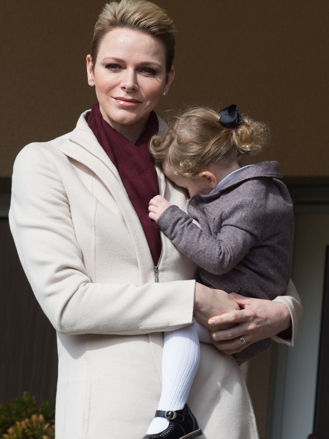 Princess Charlene in a white coat holding her toddler daughter