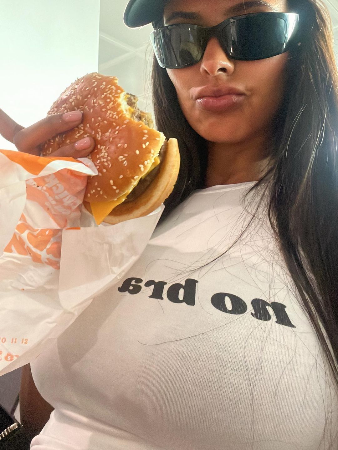 Maya Jama eats a cheeseburger in a graphic tee