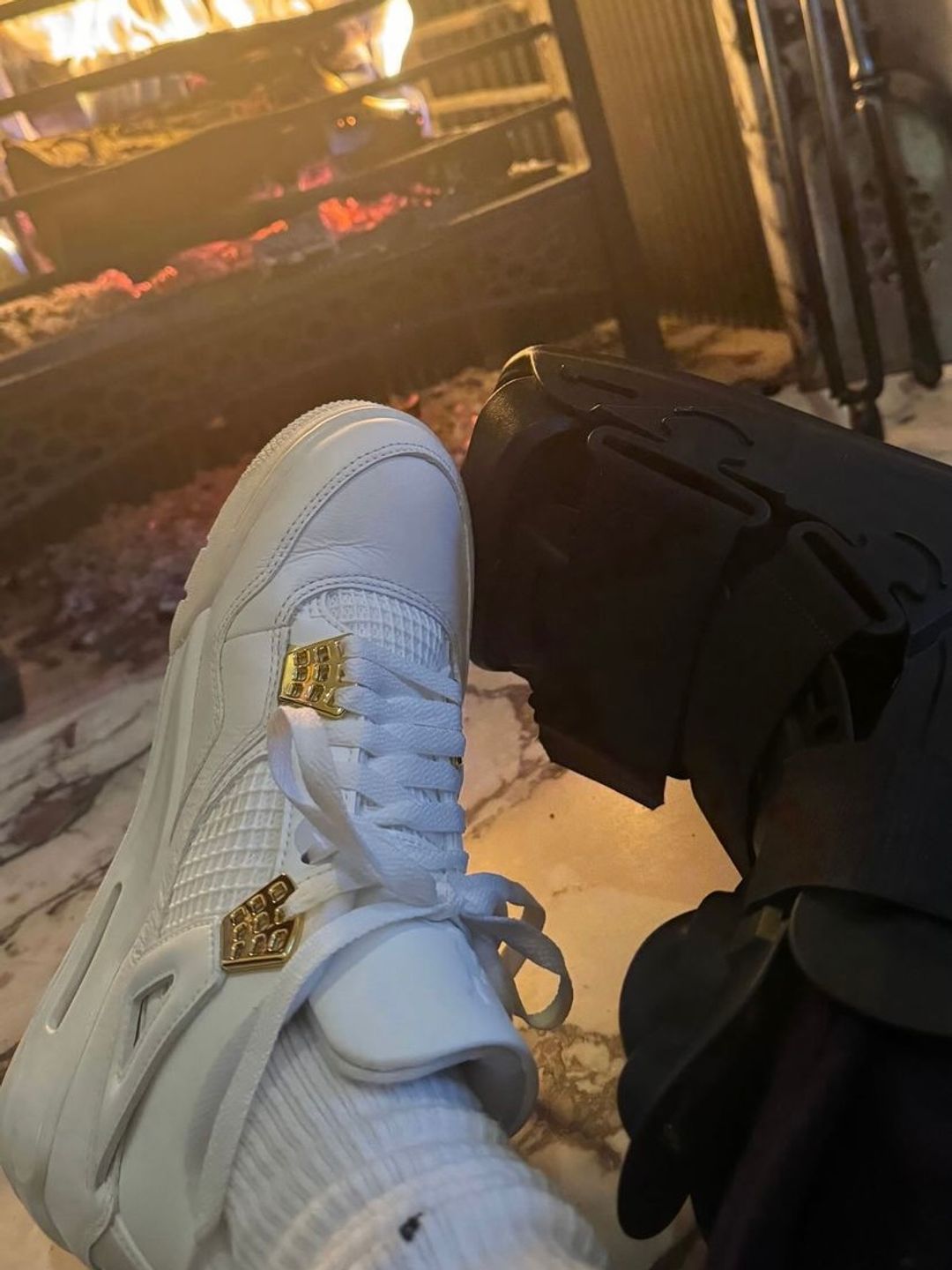 Nike Air Jordan 4 Retro Trainer alongside medical boot in front of a fireplace 