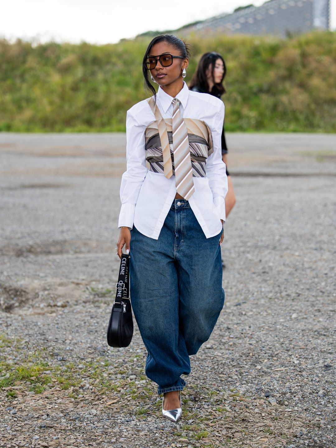 Sarah Ndiaye wears wide leg denim jeans, black Celine bag, white button shirt, corset, tie, sunglasses, silver pointed heels outside Han KjÃ¸benhavn at Copenhagen Fashion Week. 