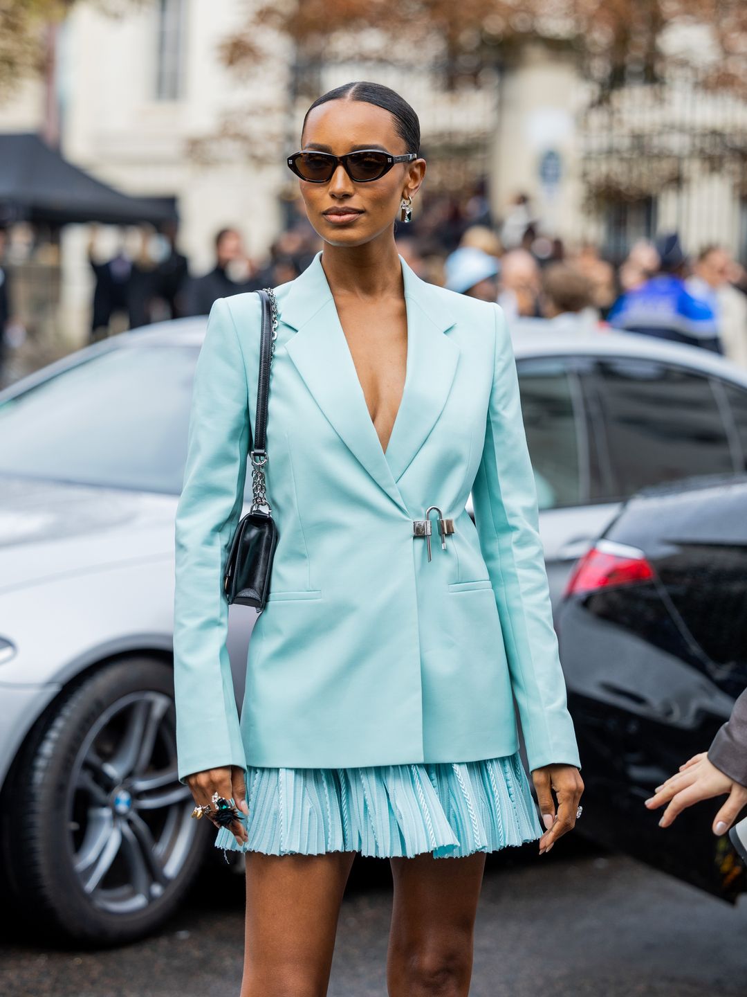A Paris Fashion Week guest wears turquoise blazer with a pleated mini skirt