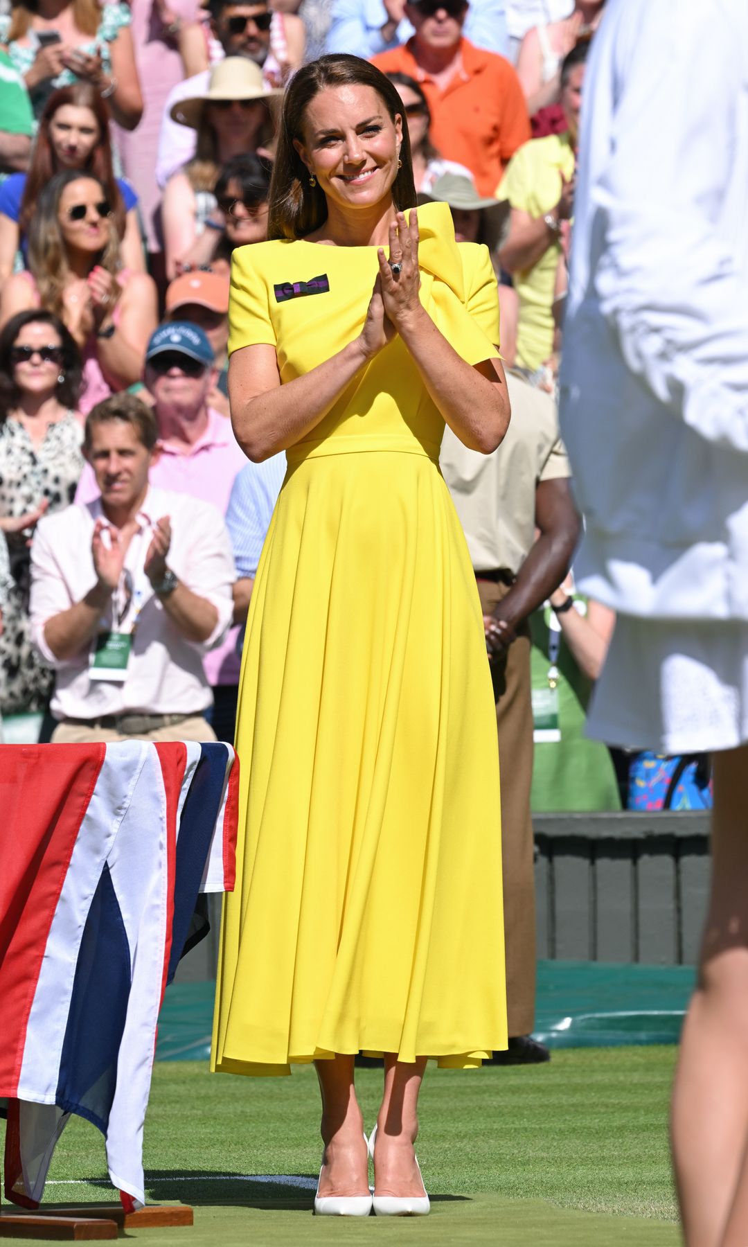 Kate Middleton at Wimbledon, 2022 clapping on the lawn, wearing a bright yellow dress and red heels
