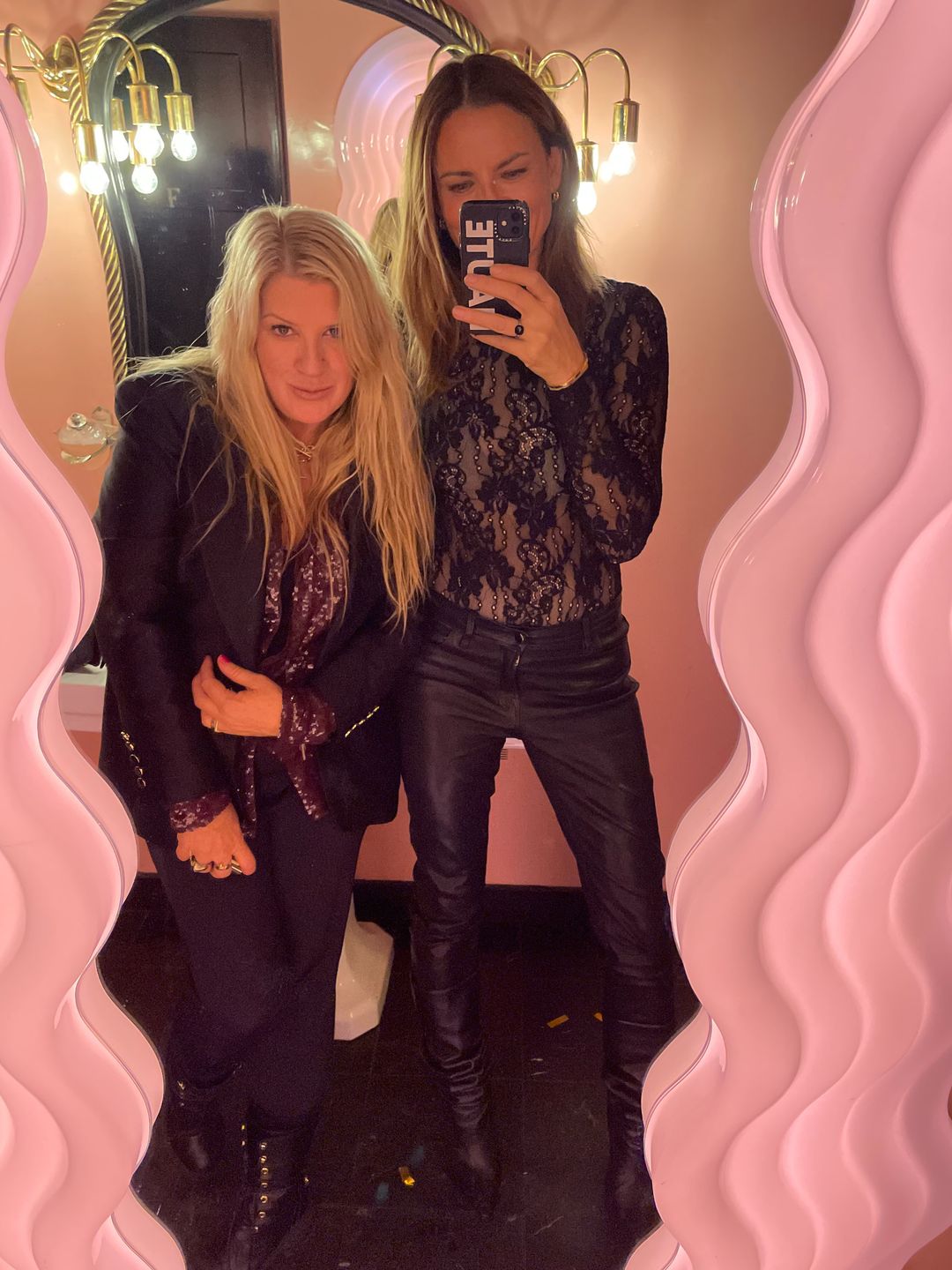 Gabriele Hackworthy poses with a friend in a mirror wearing a black lace bodysuit and leather pants