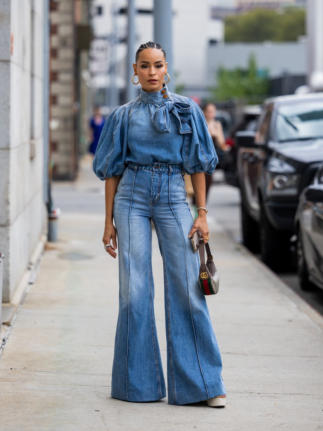 A Fashion Week guest wears high-waisted flare jeans with a denim asymmetric pussy bow blouse 