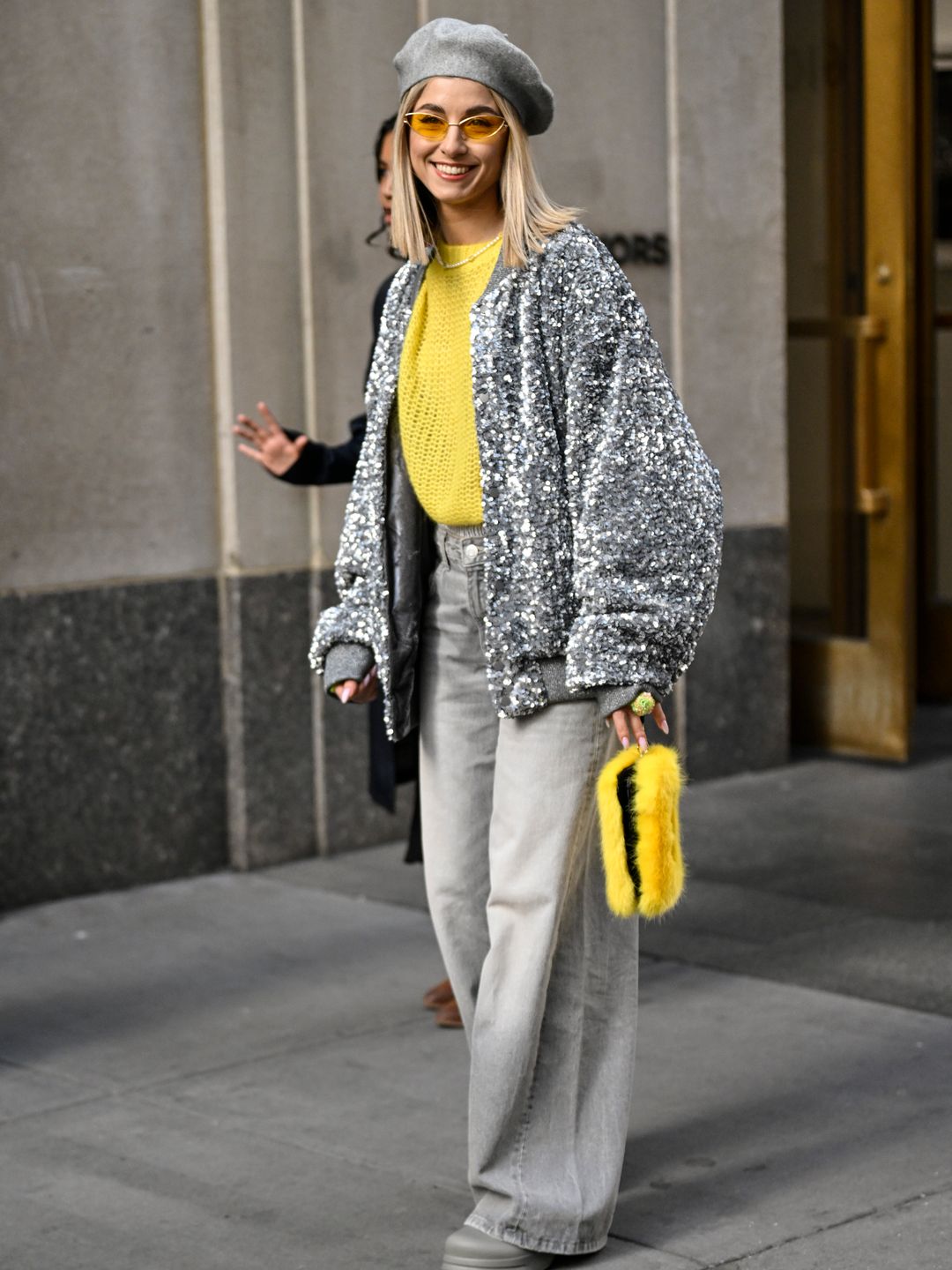 Olga Slobodianik is seen wearing a silver sequin bomber jacket, a bold-hued yellow sweater, grey jeans, a grey beret and a fluffy yellow bag outside the Collina Strada show.