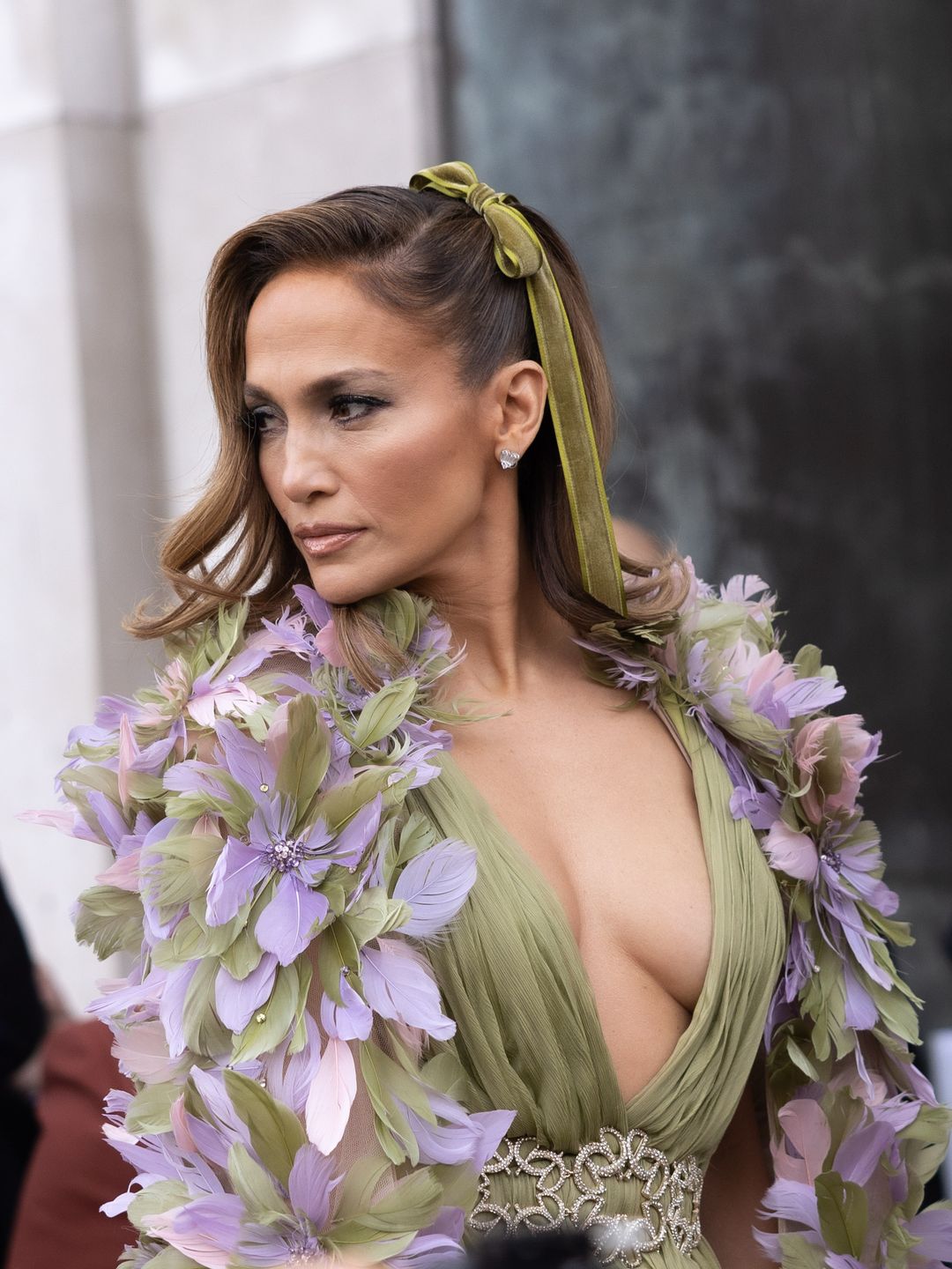 Jennifer Lopez attends the Elie Saab Haute Couture Spring/Summer show wearing a green bow in her hair to match her green gown and feathered cape