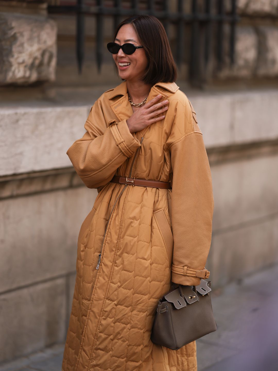 In September Aimee Song was spotted outside the Hermès SS24 show wearing a camel coloured oversized padded coat paired with a taupe Hermès Birkin 