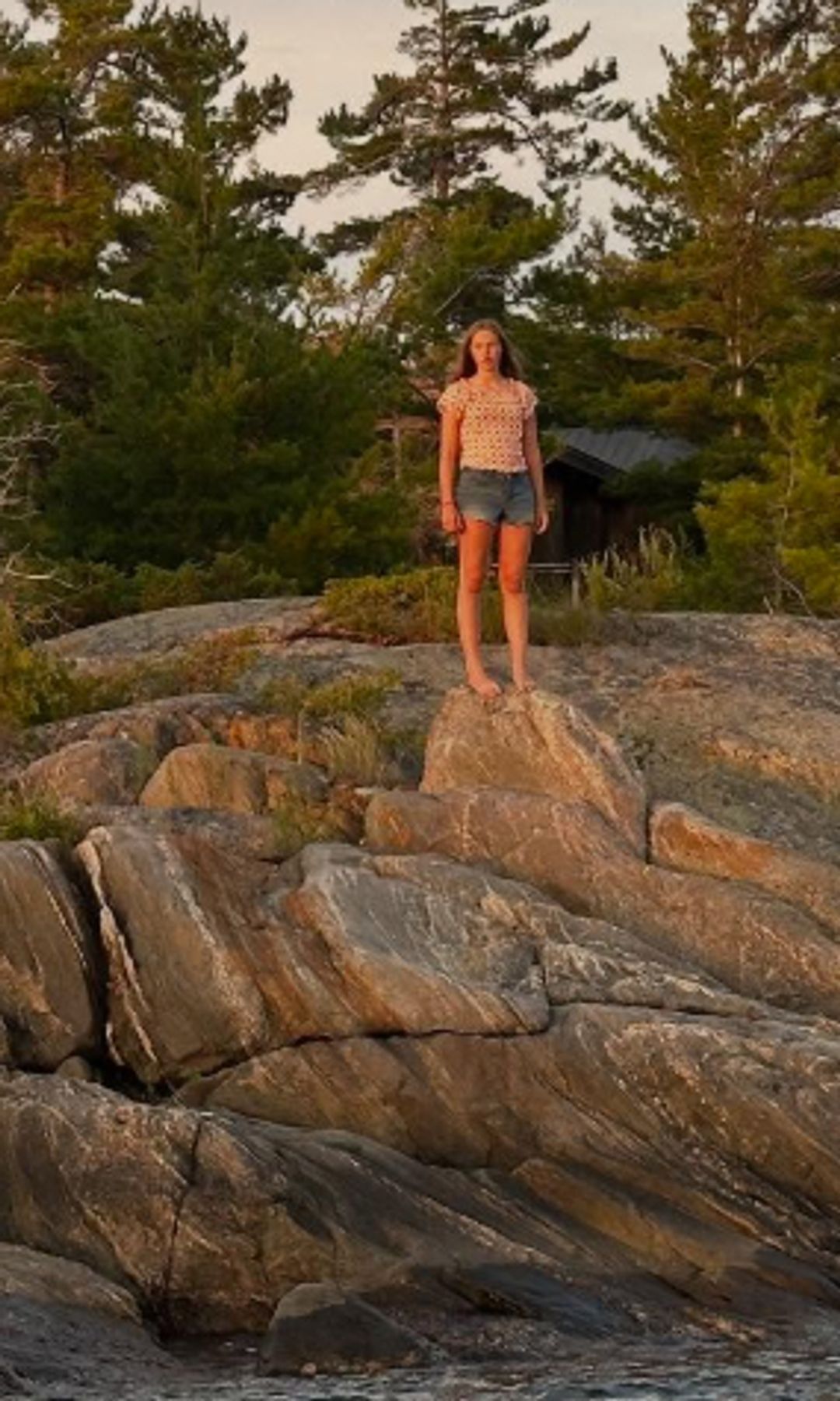 Une adolescente debout sur des rochers avec un coucher de soleil