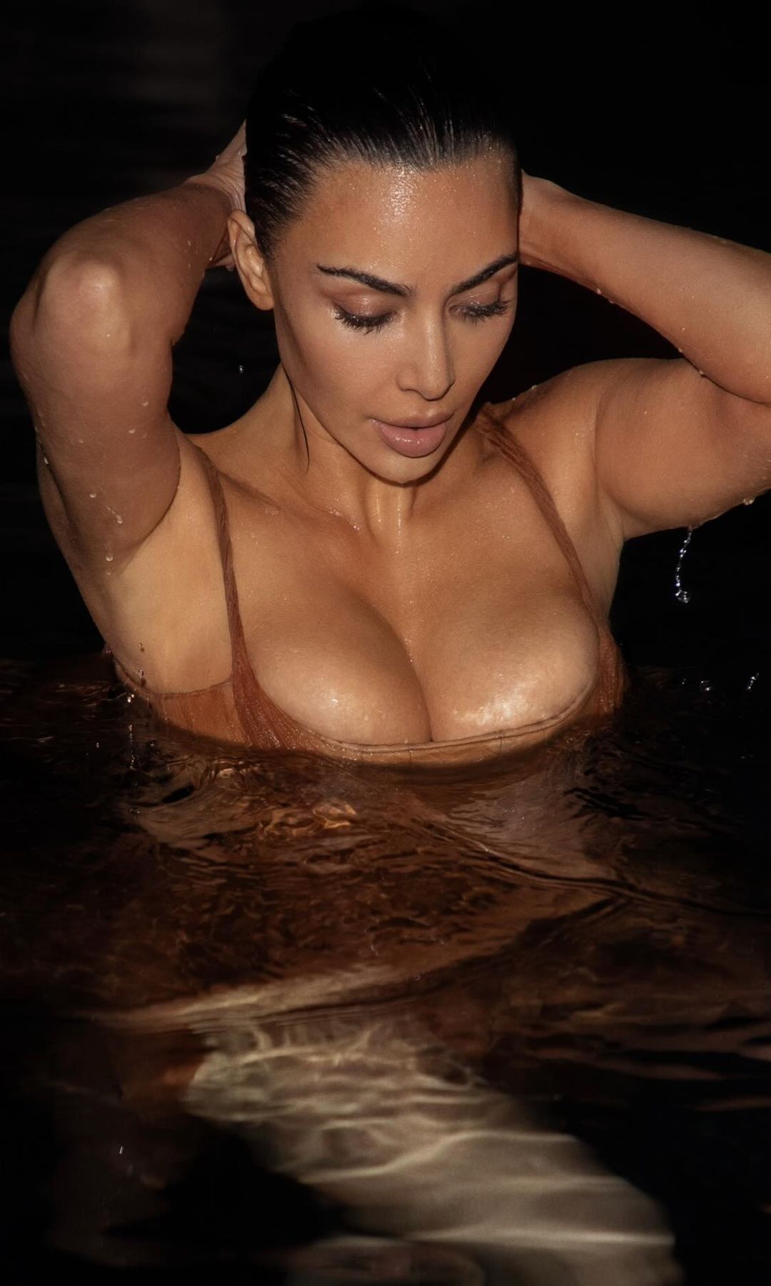 Kim Kardashian poses in the ocean wearing a tulle brown designer dress