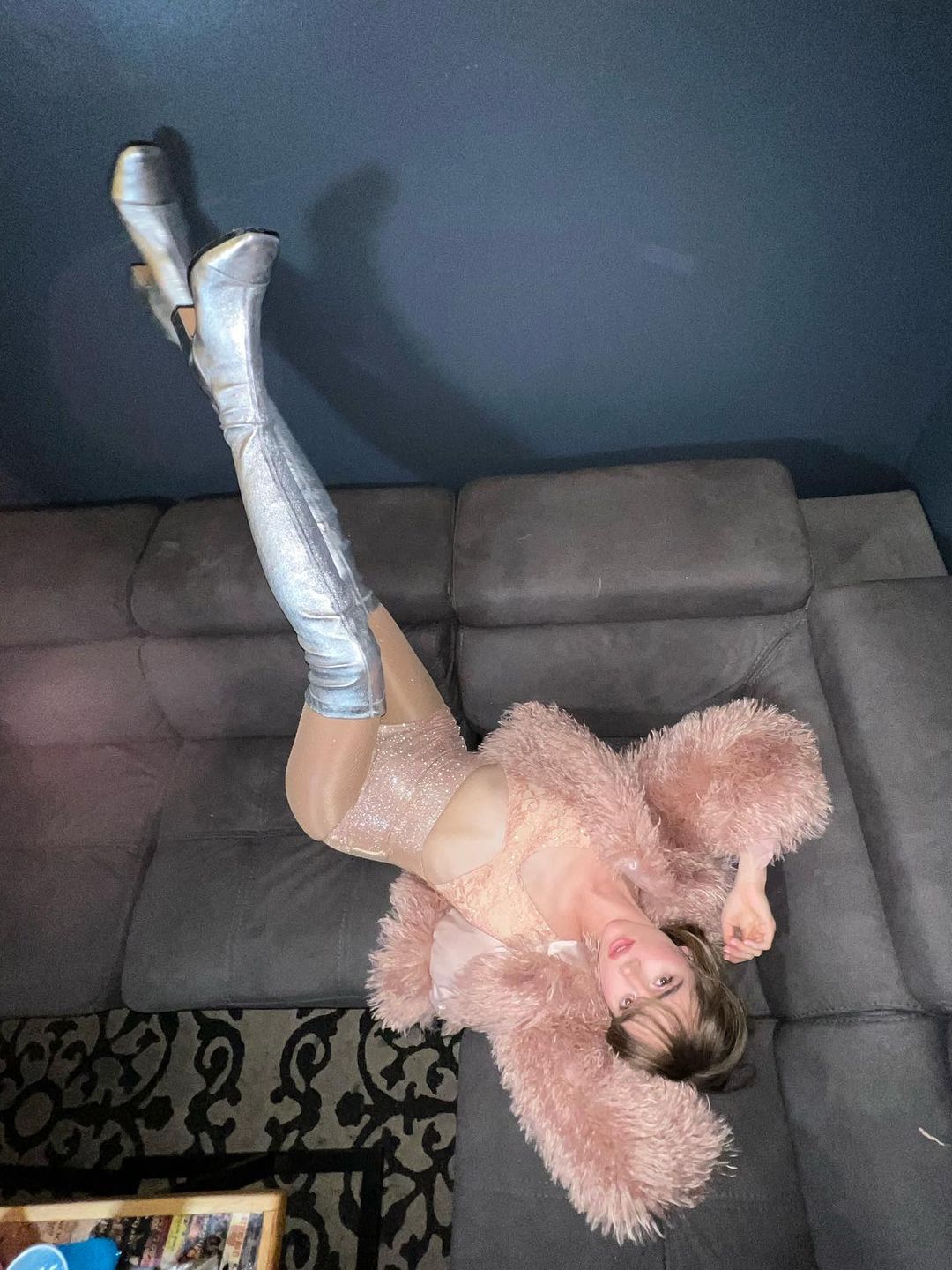 Suki Waterhouse poses on a couch in thigh-high silver boots and a fluffy pink jacket