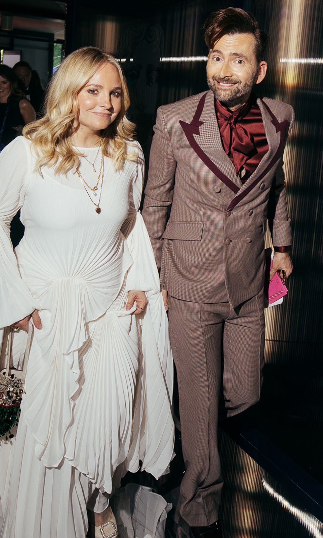 Georgia Tennant holding up her white dress as she walks alongside smiling David Tennant