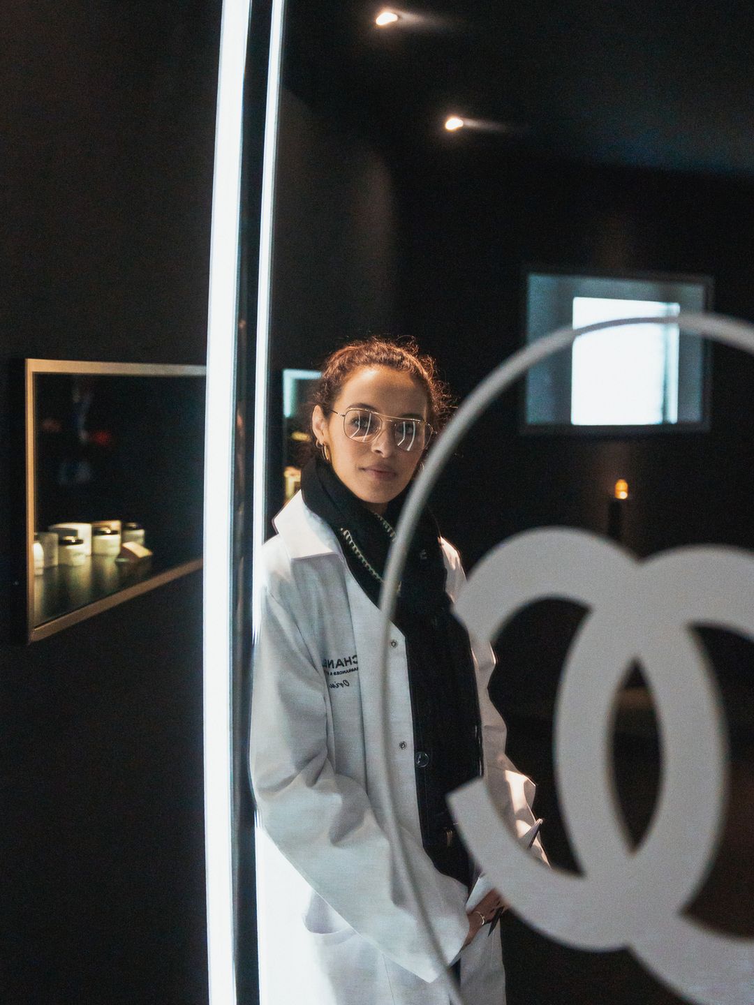 Orin Carlin wearing Chanel lab coat in front of double C mirror 