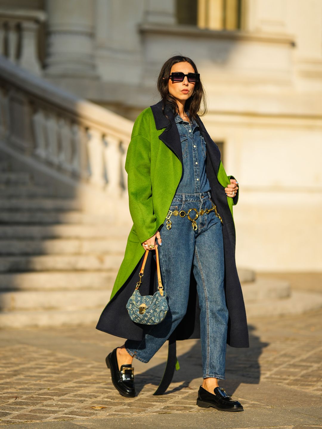 PARIS, FRANCE - NOVEMBER 10: Gabriella Berdugo wears a blue denim shirt from Wrangler, matching blue denim jeans pants from Wrangler, a vintage golden chain belt, black leather loafer shoes with buckle from Roger Vivier, a blue denim vintage Louis Vuitton bag with printed logo monogram, a reversible green and blue long coat from Essentiel Antwerp, during a street style fashion photo session, on November 10, 2021 in Paris, France. (Photo by Edward Berthelot/Getty Images)