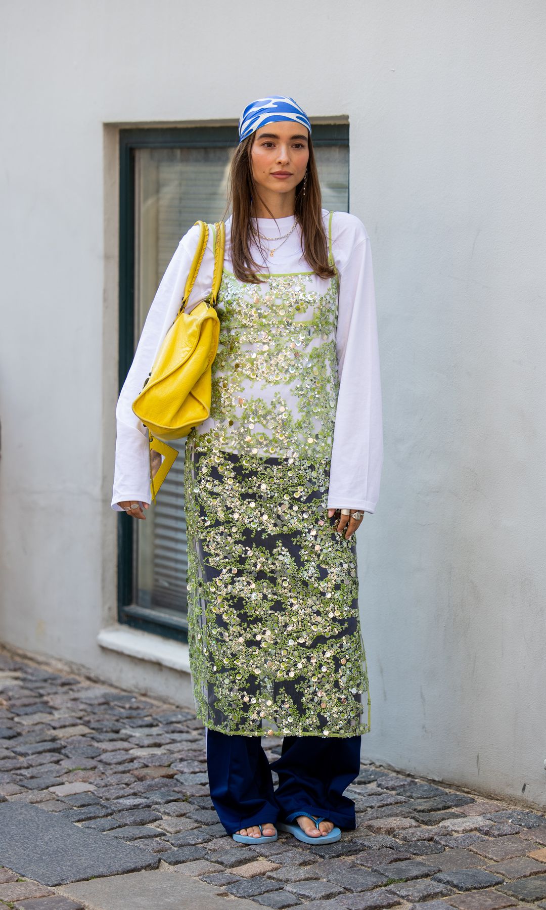 Evi Wave wears head scarf, green transparent sequined dress, white long sleeve shirt, yellow bag outside Rave Review during Copenhagen Fashion Week day two on August 05, 2025 in Copenhagen, Denmark