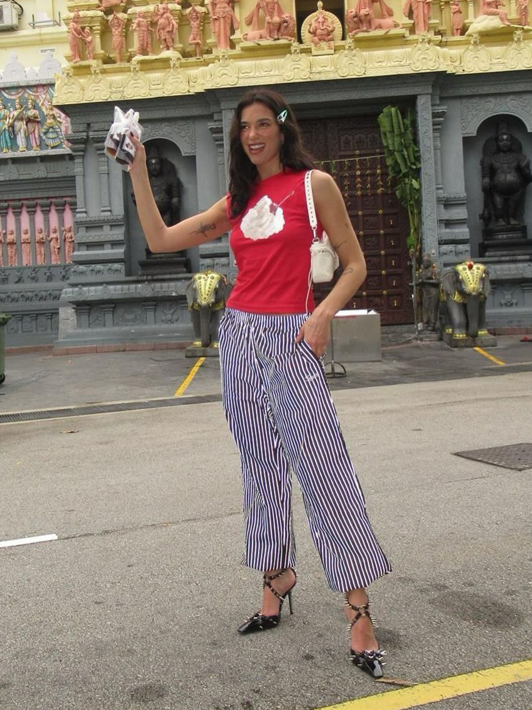 Dua Lipa poses in striped pants, black heels and a red vest while in Singapore