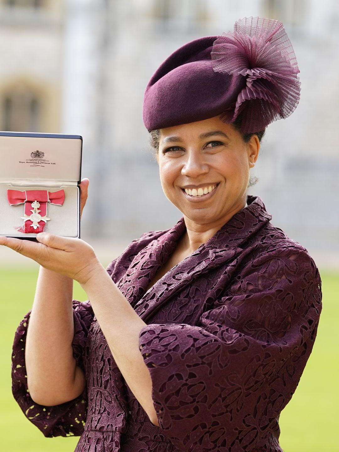 Margherita Taylor in a plum-coloured dress holding an MBE
