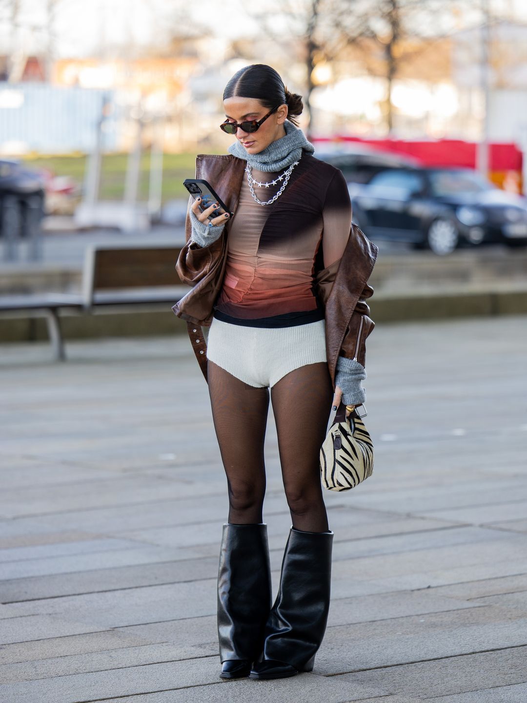 A guest wears white micro shorts, tights, brown top, animal print bag, black boots and a grey scarf 