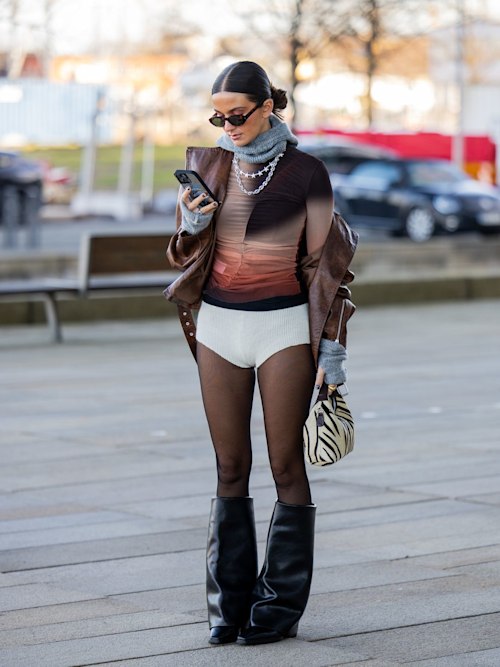 A guest wears white micro shorts, tights, brown top, animal print bag, black boots and a grey scarf 