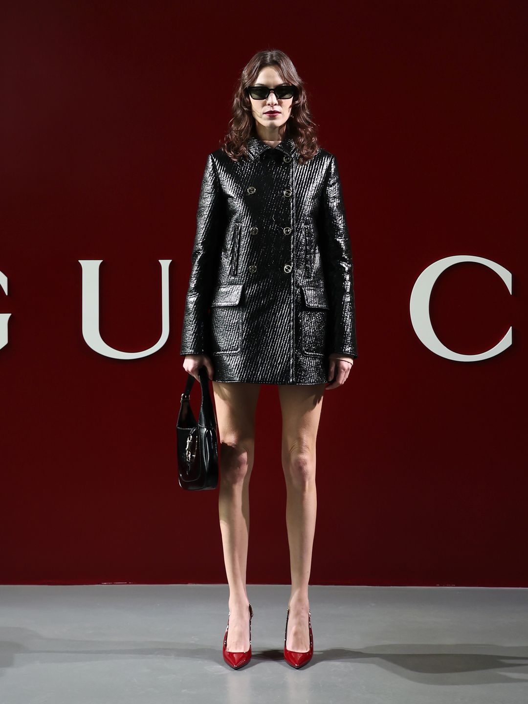 Alexa Chung wore a certified cool-girl ensemble to the Gucci show. Pairing a black patent coat mini dress with red heels and a Gucci Jackie bag.