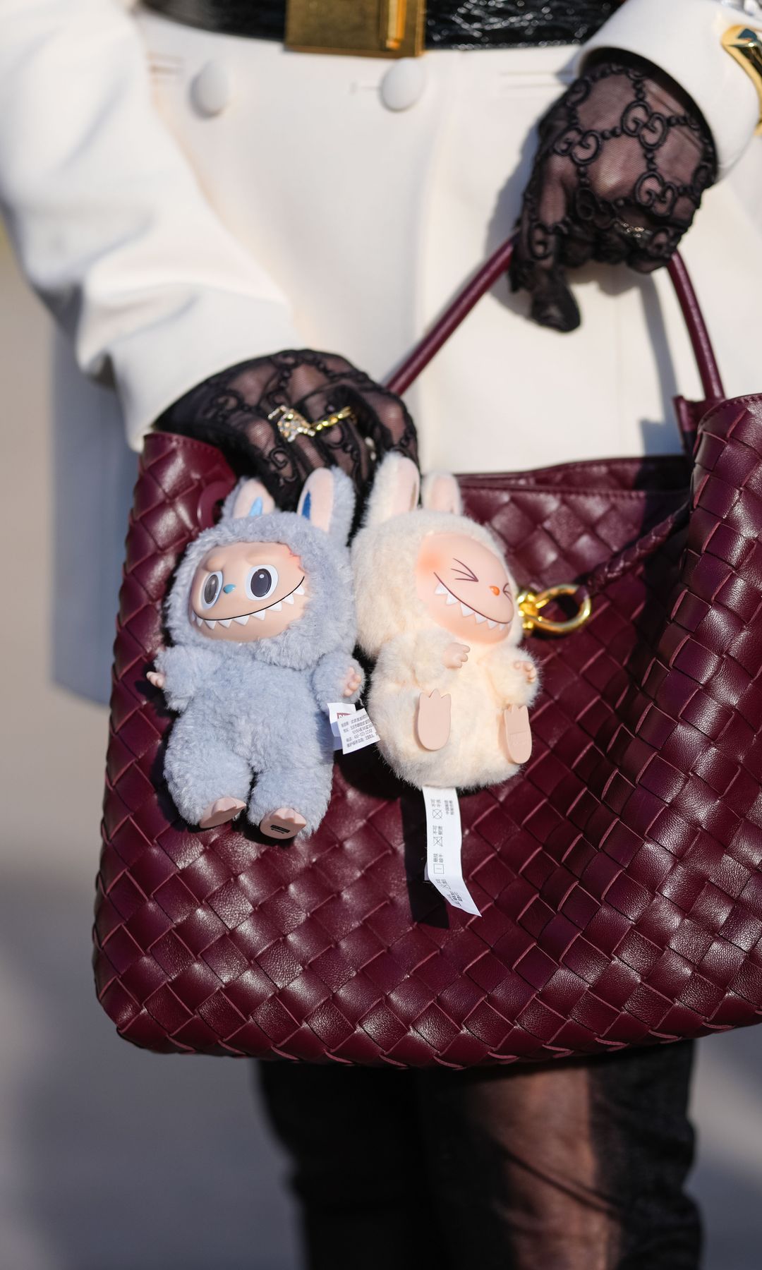 A guest wears a burgundy bordeaux woven Bottega Veneta Andiamo leather bag, light blue Labubu bag charm, cream Labubu bag charm, outside Elie Saab, during the Paris Fashion week Women's Fall/Winter 2025-2026 on March 8, 2025 in Paris, France