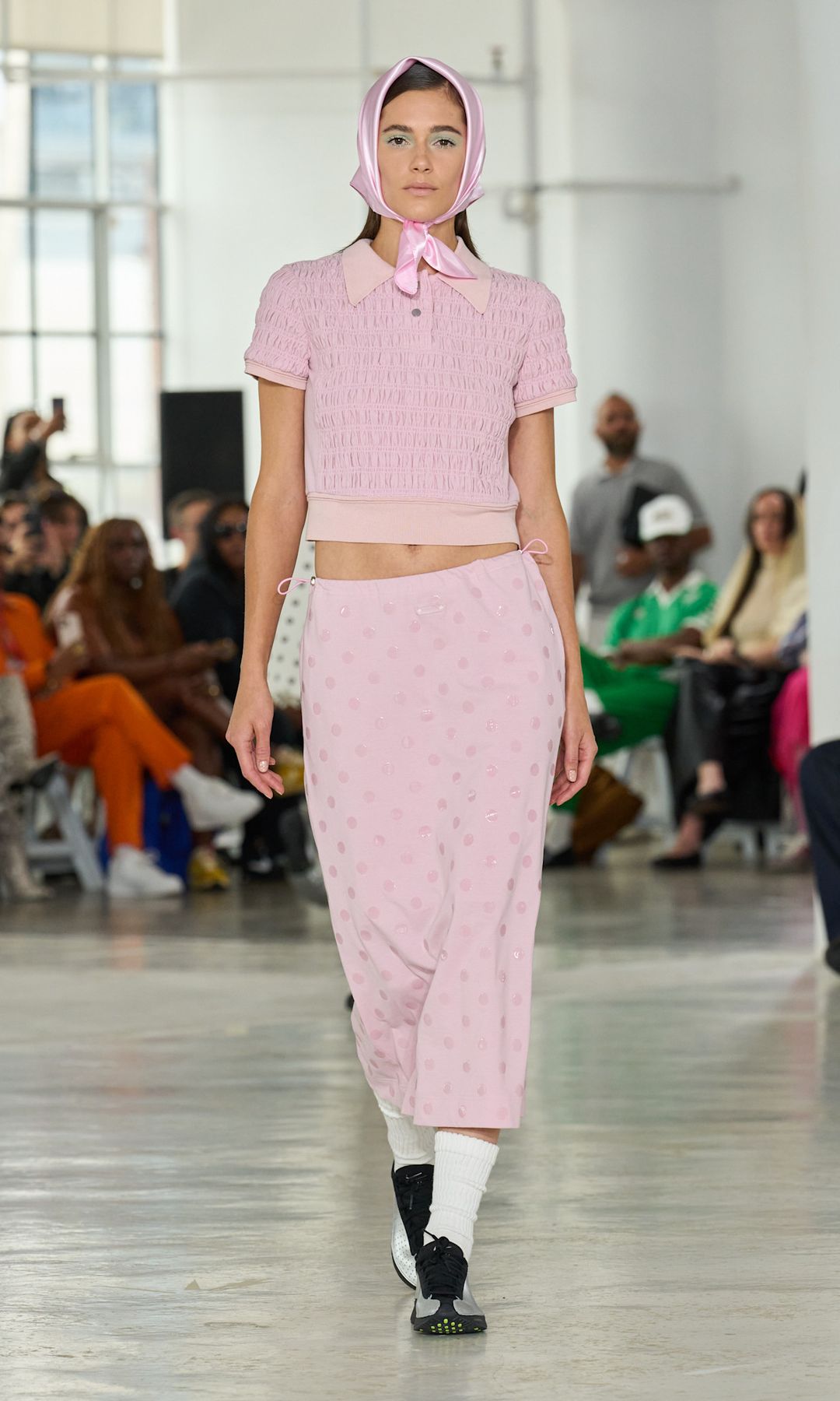 A model walks the runway at Private Policy wearing a baby pink polo top, midi skirt and headscarf, teamed with white socks and trainers