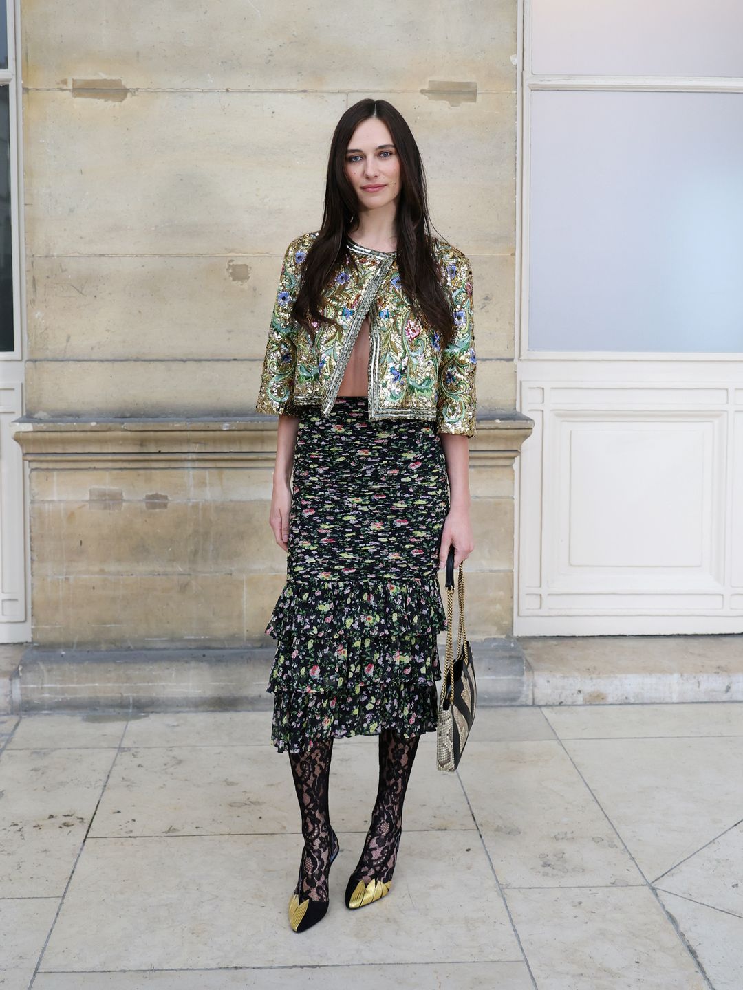 Devon Lee Carlson paired a ruffled floral skirt with lace tights, gold-tipped heels, and a heavily embellished cropped jacket, creating a bold fusion of boho-chic and high fashion.