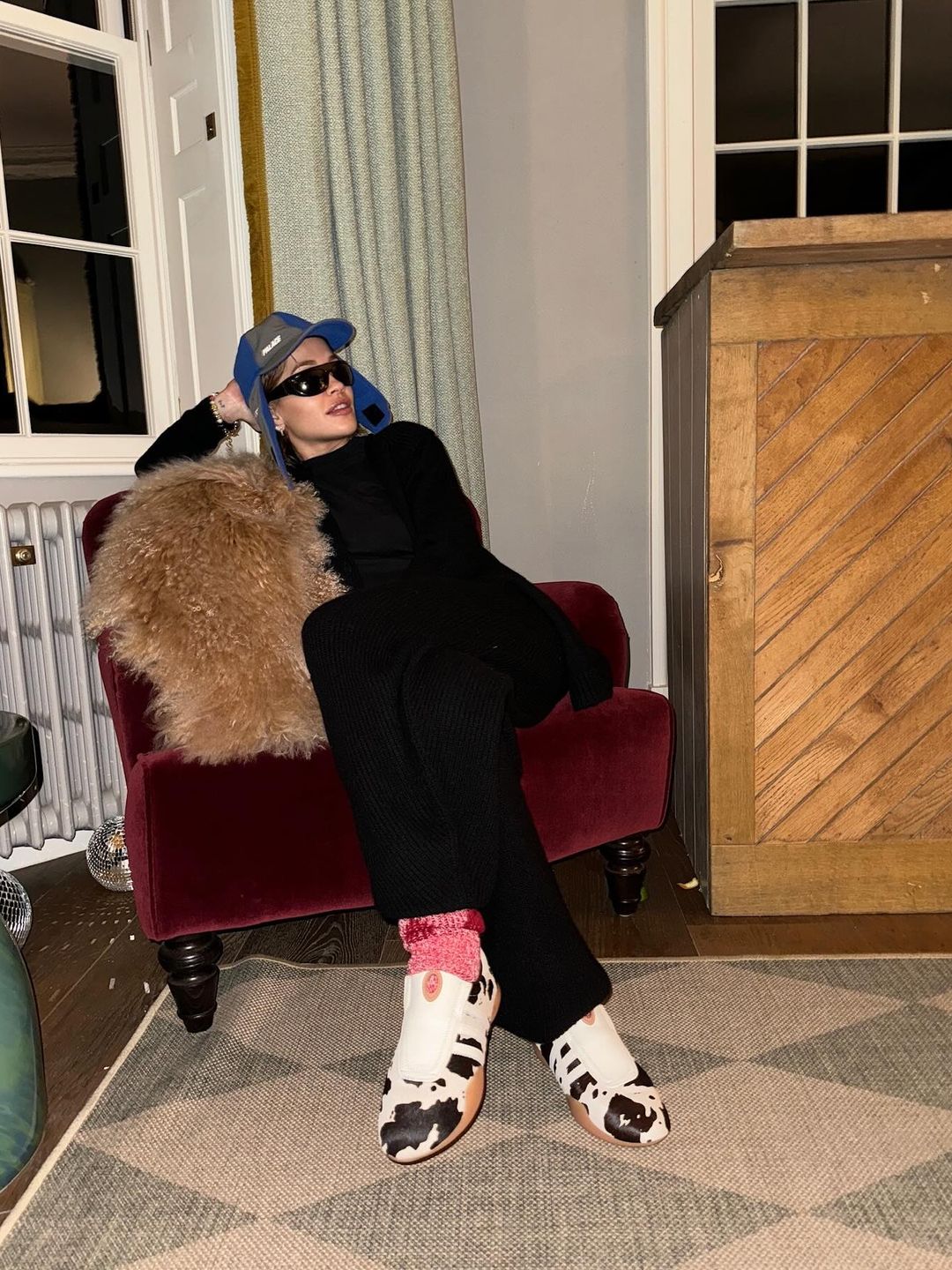 Rita Ora poses in a black tracksuit, hat and cow print sneakers